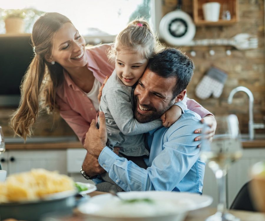 Young happy parents embracing with their small daughter during lunch at dining table.