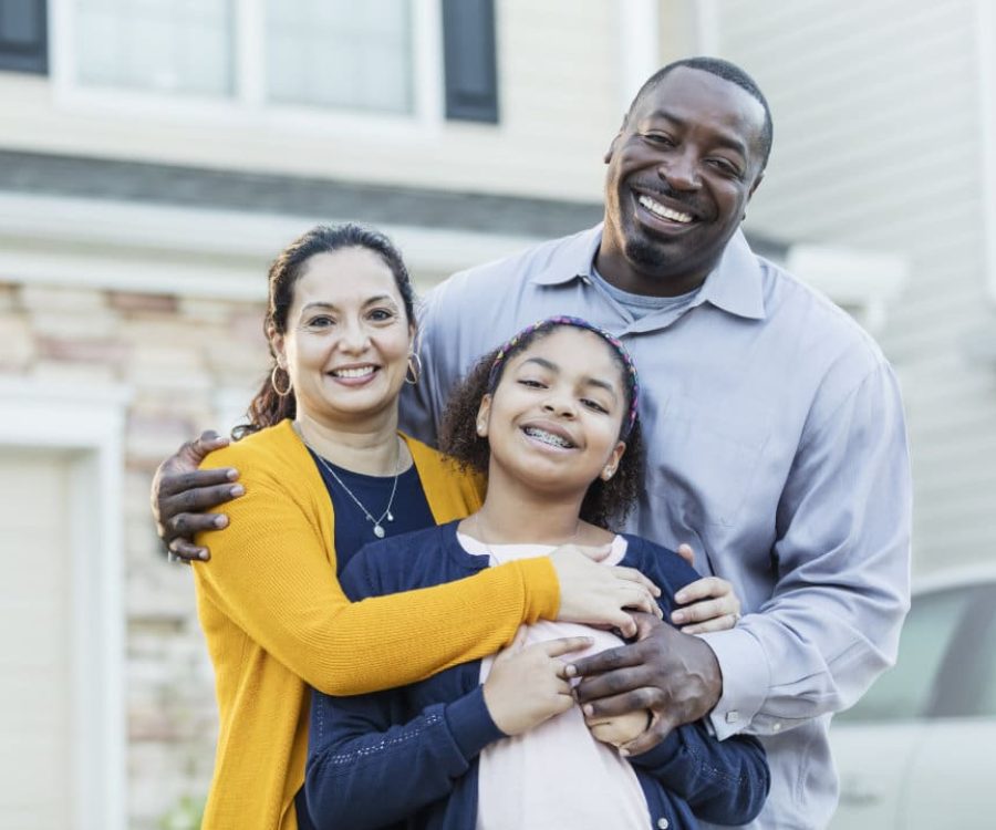 An 11 year old mixed race Hispanic and African-American girl standing with her parents outside their home. Mom is a mature Hispanic woman and dad is a mature African-American man. They are both in their 40s, happy and proud of their daughter.  All are smiling at the camera.